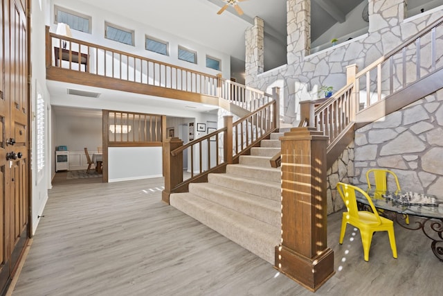 staircase featuring visible vents, ceiling fan, baseboards, wood finished floors, and high vaulted ceiling