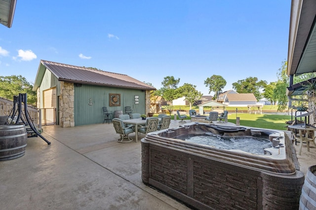 view of patio featuring a detached garage, fence, outdoor dining area, and a hot tub