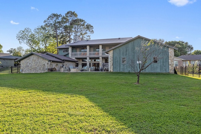 rear view of property with a ceiling fan, a yard, stone siding, and fence