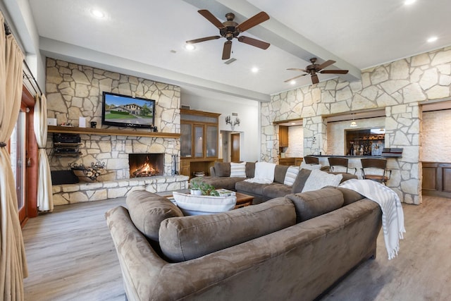 living area with light wood-style floors, a ceiling fan, beam ceiling, and a fireplace