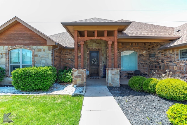 entrance to property with roof with shingles, covered porch, and stone siding