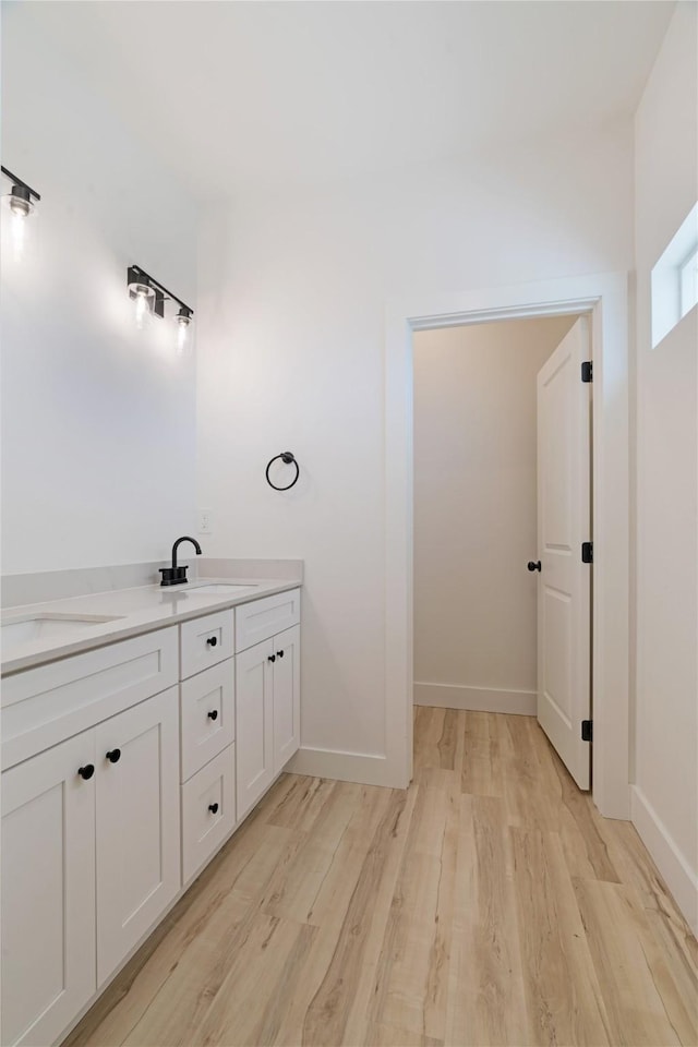 full bath featuring baseboards, wood finished floors, double vanity, and a sink