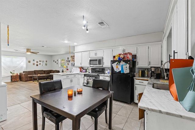 kitchen with freestanding refrigerator, stainless steel microwave, gas range oven, a textured ceiling, and light tile patterned flooring