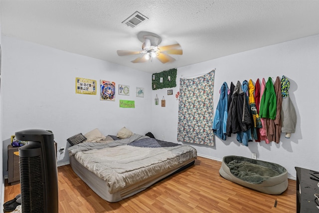 bedroom with a ceiling fan, visible vents, baseboards, a textured ceiling, and wood finished floors