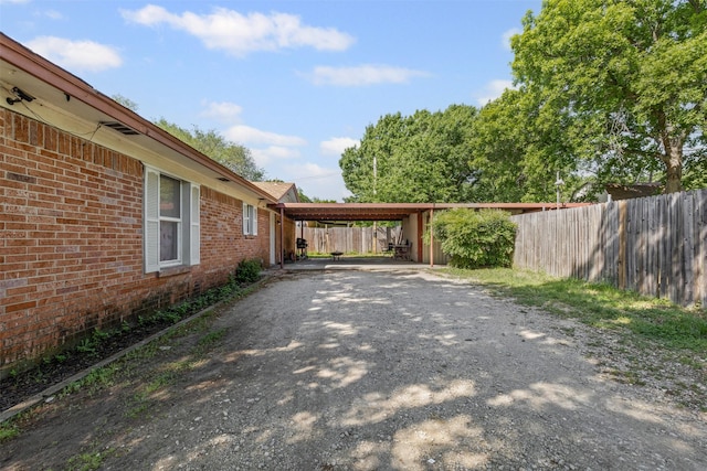 exterior space featuring fence, driveway, an attached carport, and brick siding