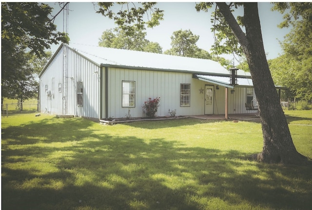 back of house featuring a lawn, fence, board and batten siding, and metal roof