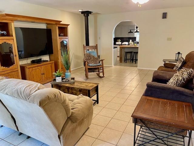 living area with arched walkways, baseboards, light tile patterned floors, and a wood stove