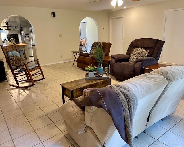 living room with baseboards, arched walkways, ceiling fan, and light tile patterned floors