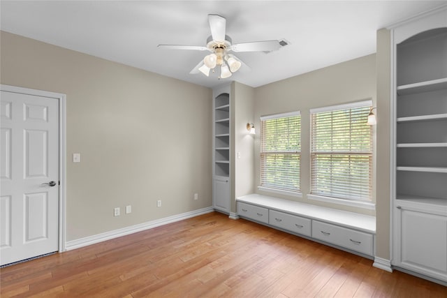 unfurnished room with light wood-type flooring, a ceiling fan, built in features, and baseboards
