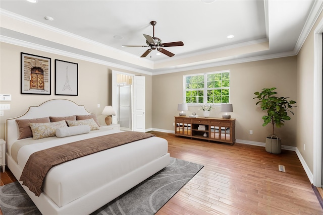 bedroom with light wood finished floors, ceiling fan, a raised ceiling, crown molding, and baseboards