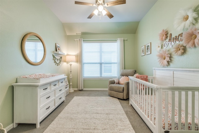 bedroom with a ceiling fan, a nursery area, vaulted ceiling, light carpet, and baseboards
