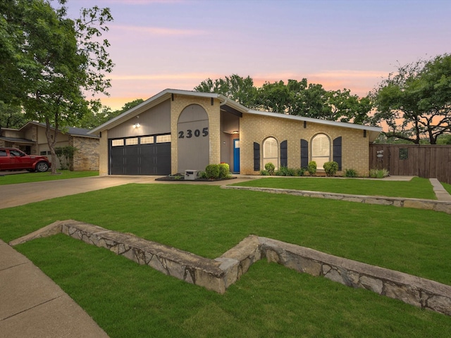 mid-century modern home featuring a garage, a yard, brick siding, concrete driveway, and fence