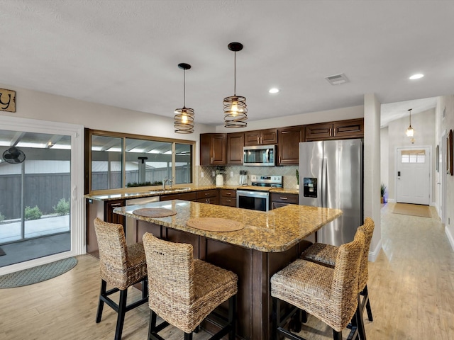 kitchen with light wood finished floors, a sink, decorative backsplash, visible vents, and appliances with stainless steel finishes