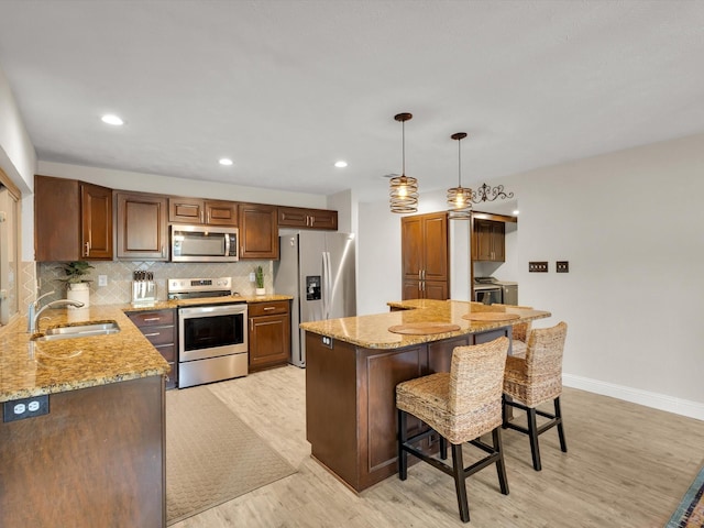 kitchen featuring light stone counters, a breakfast bar, stainless steel appliances, a sink, and light wood-type flooring