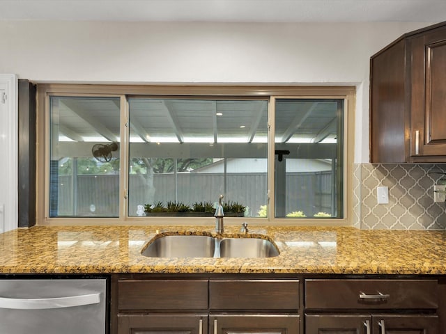kitchen featuring tasteful backsplash, stainless steel dishwasher, a sink, dark brown cabinetry, and light stone countertops