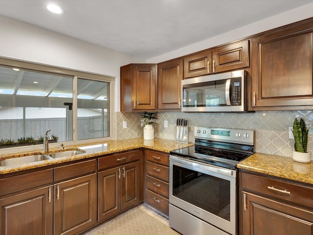 kitchen with appliances with stainless steel finishes, backsplash, light stone countertops, and a sink