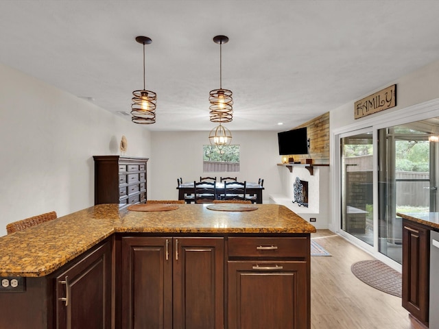 kitchen featuring light stone countertops, decorative light fixtures, dark brown cabinets, and light wood-style floors