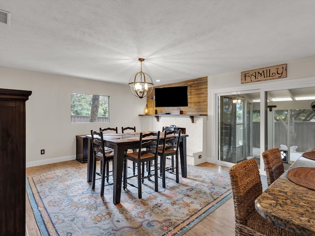 dining area featuring a notable chandelier, light wood-type flooring, visible vents, baseboards, and a textured ceiling