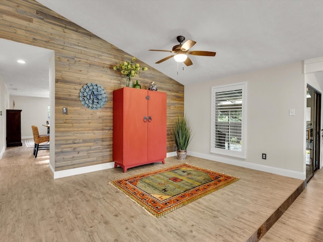 interior space featuring wood finished floors, wood walls, baseboards, high vaulted ceiling, and a ceiling fan
