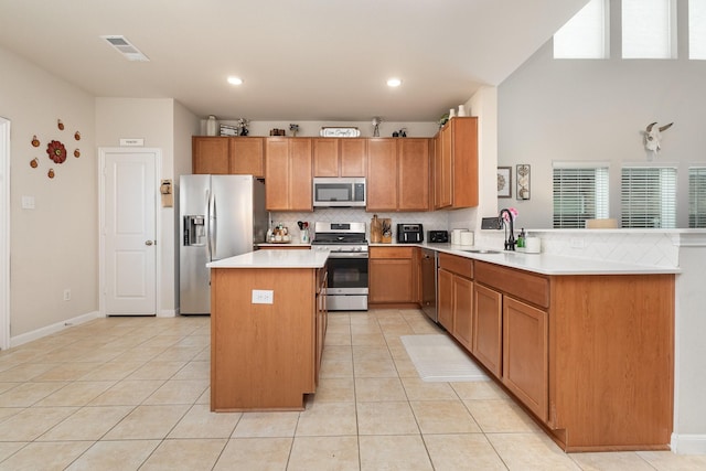 kitchen with a sink, appliances with stainless steel finishes, light countertops, a center island, and backsplash