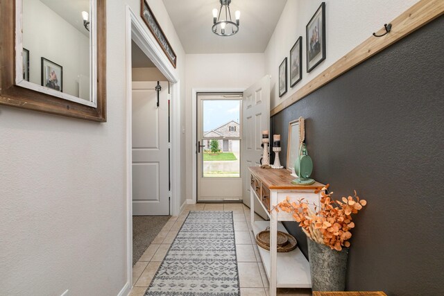 doorway featuring light tile patterned floors, a notable chandelier, a textured wall, and baseboards