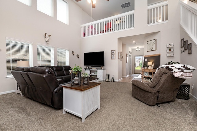 living area featuring light carpet, baseboards, visible vents, a ceiling fan, and a towering ceiling