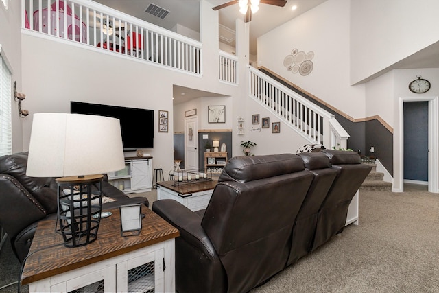 carpeted living room featuring stairway, visible vents, a ceiling fan, and a high ceiling