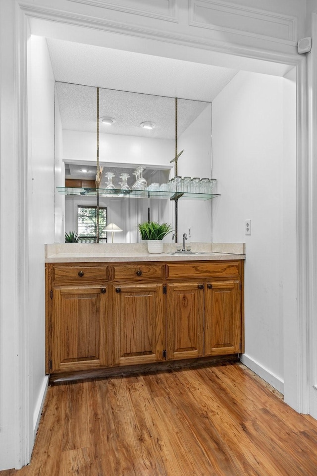 bar featuring a sink, wood finished floors, and baseboards
