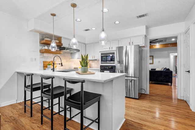 kitchen with a textured ceiling, appliances with stainless steel finishes, visible vents, a peninsula, and backsplash