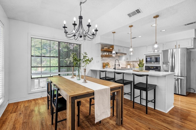 dining space featuring wood finished floors, visible vents, a chandelier, and a textured ceiling