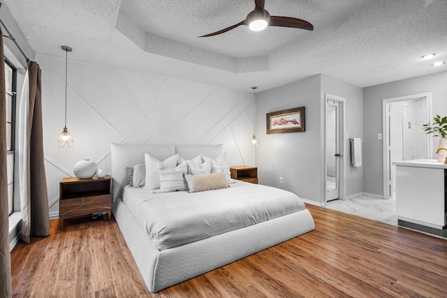 bedroom with ensuite bath, light wood-style flooring, ceiling fan, baseboards, and a textured ceiling