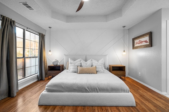 bedroom featuring wood finished floors, baseboards, visible vents, a raised ceiling, and a textured ceiling