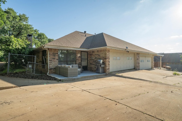 view of side of property with brick siding, fence, a garage, driveway, and outdoor lounge area