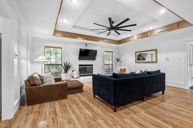 living area featuring light wood finished floors, a ceiling fan, a raised ceiling, and plenty of natural light