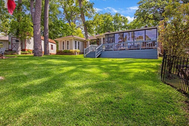 rear view of property featuring fence, a yard, a wooden deck, and a sunroom
