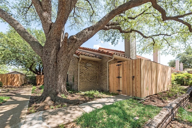 exterior space featuring a tile roof, a chimney, a gate, brick siding, and fence
