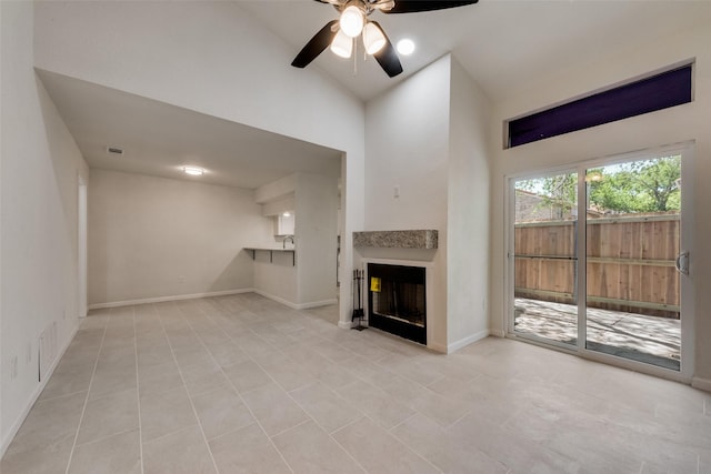 unfurnished living room with ceiling fan, a fireplace, baseboards, high vaulted ceiling, and light tile patterned flooring