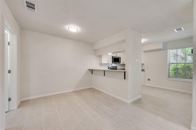 kitchen featuring visible vents, white cabinets, light countertops, and stainless steel microwave