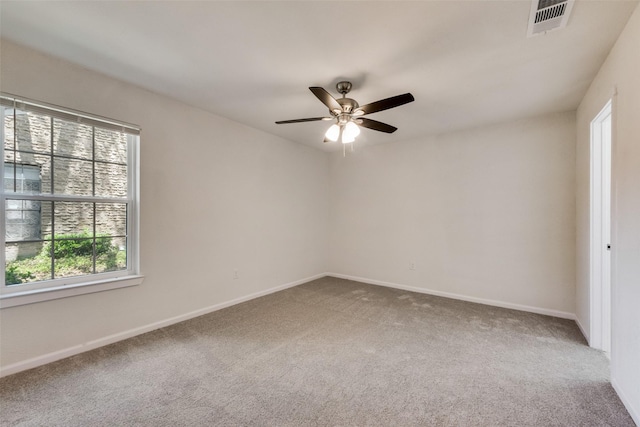 carpeted empty room featuring a wealth of natural light, ceiling fan, visible vents, and baseboards