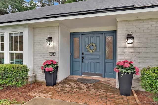 property entrance featuring brick siding and a shingled roof