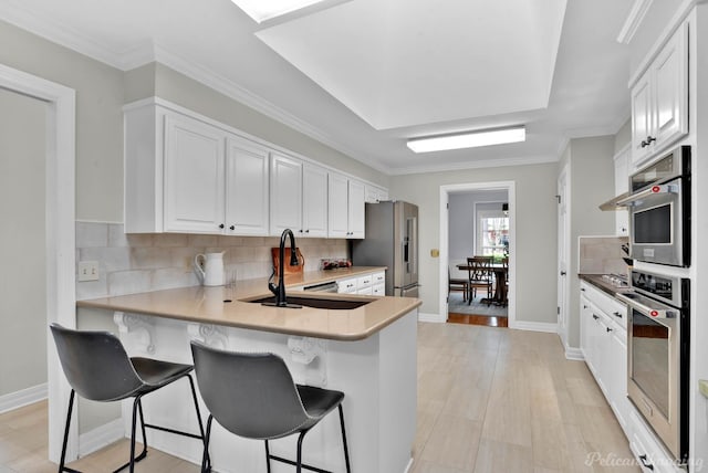 kitchen featuring a sink, tasteful backsplash, a kitchen breakfast bar, high end refrigerator, and white cabinetry