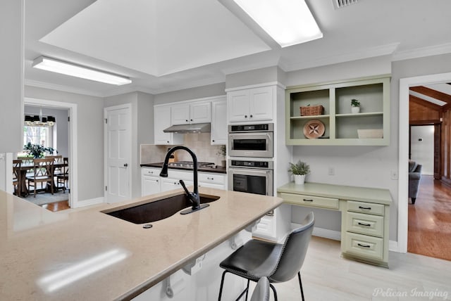 kitchen with a sink, under cabinet range hood, crown molding, white cabinets, and backsplash
