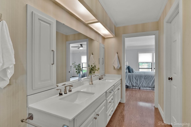 ensuite bathroom featuring wallpapered walls, wood finished floors, double vanity, ceiling fan, and baseboards