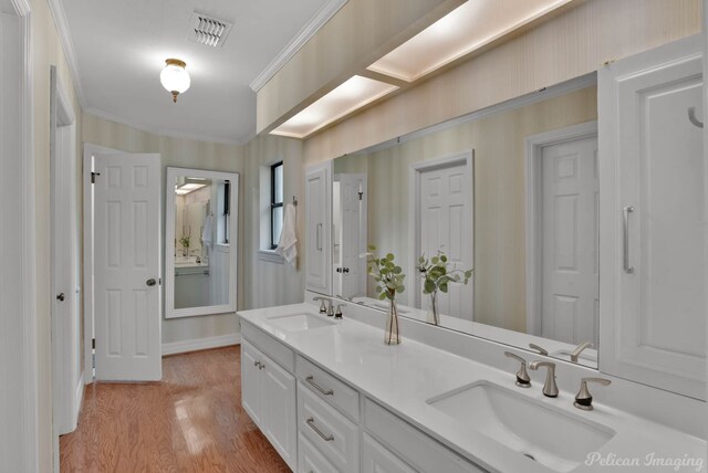 full bathroom featuring ornamental molding, wood finished floors, double vanity, and wallpapered walls