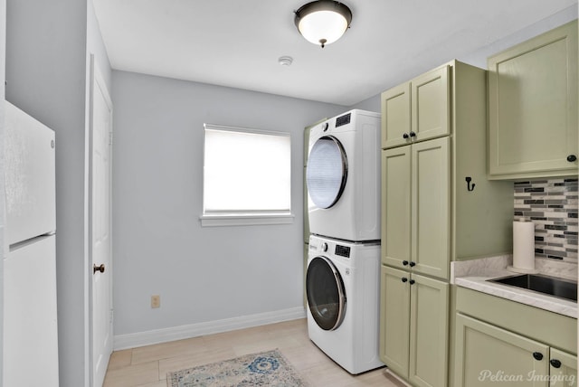 laundry room featuring stacked washer and clothes dryer, cabinet space, and baseboards