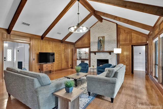 living room featuring light wood-type flooring, high vaulted ceiling, beam ceiling, a brick fireplace, and wooden walls