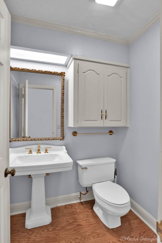 bathroom with baseboards, toilet, wood finished floors, and ornamental molding