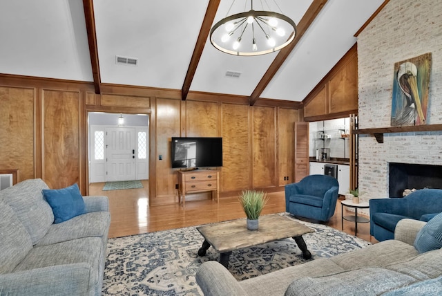 living area featuring light wood-style floors, beam ceiling, high vaulted ceiling, wooden walls, and a brick fireplace