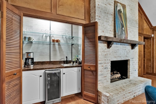 indoor wet bar with wine cooler, light wood-type flooring, and a brick fireplace