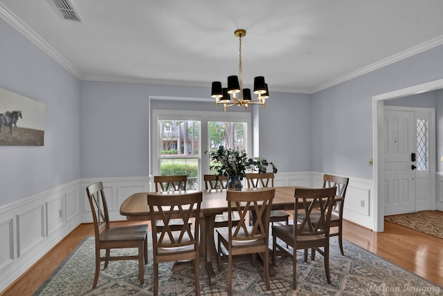 dining area with a chandelier, wood finished floors, crown molding, a wainscoted wall, and a decorative wall